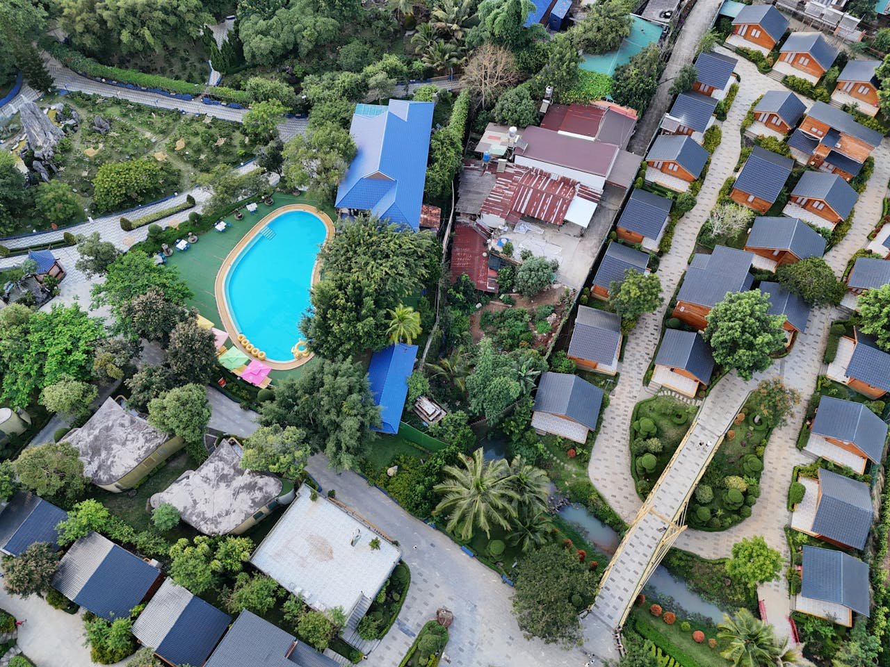 service-03 Aerial shot of a luxurious resort with a central pool, surrounded by trees and cottages.